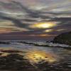 Yellow and red colours of the sun reflect in the sea past a headland
